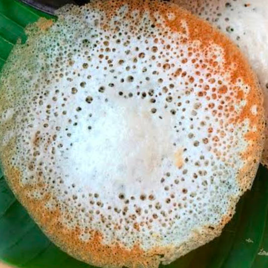 A close-up of aappam with coconut milk on a green banana leaf showcasing its lacy edges and soft center